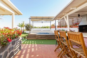 A patio with a hot tub, wooden chairs, a pergola, and potted plants.