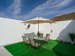A patio with a table and chairs, a large umbrella, artificial grass, and a white wall with a mural.