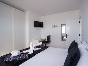 A hotel room with a bed, a desk, a chair, a TV, a coat rack, and a mirror.