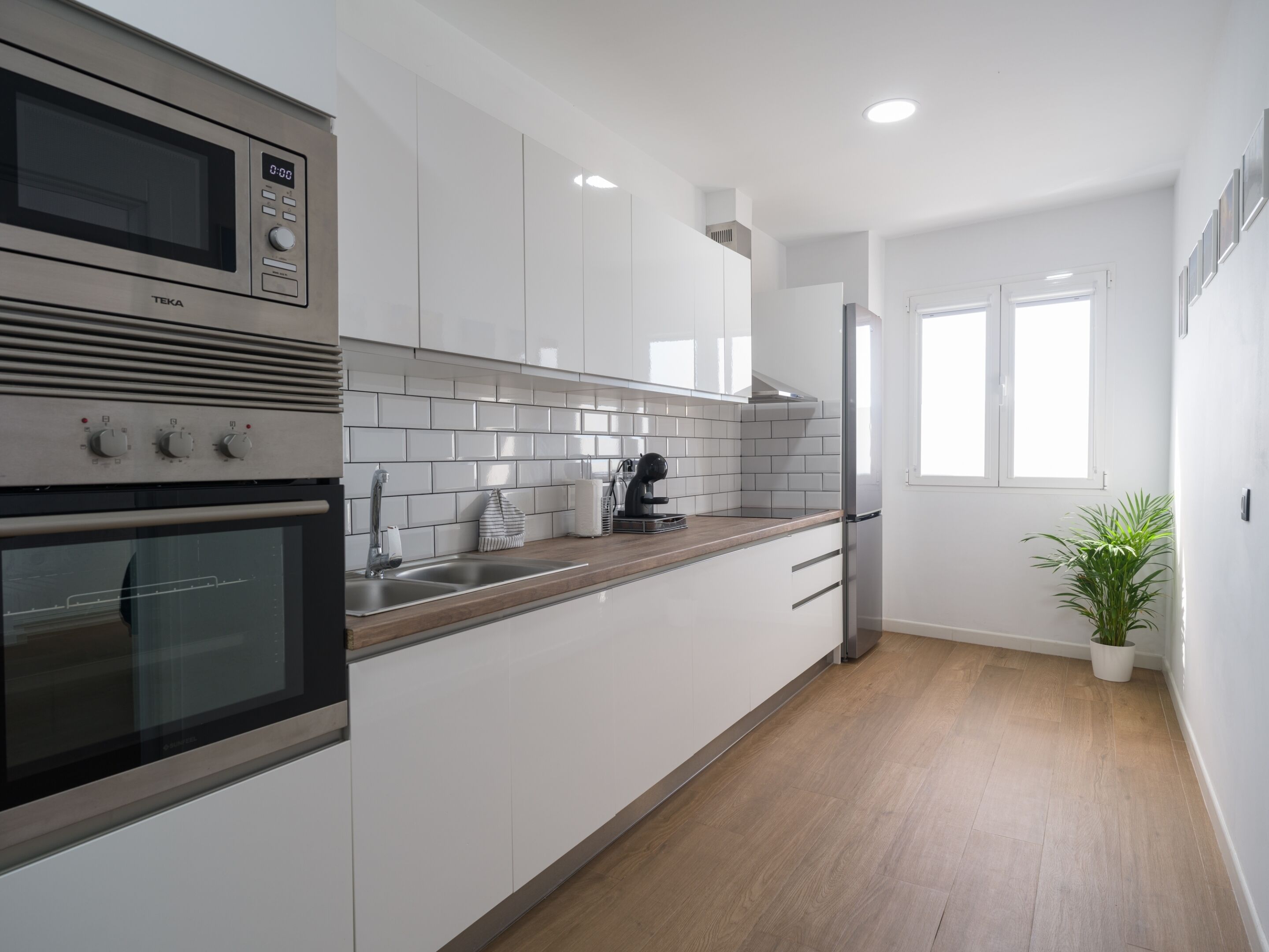 A modern kitchen with white cabinets, a stainless steel oven, a microwave, and a sink.