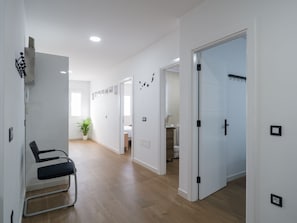 A hallway with a chair, a potted plant, and a door leading to a bathroom.
