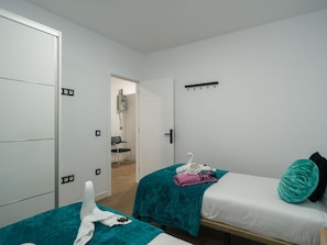 A room with two beds, a door, a coat rack, and a small bathroom visible through an open door.