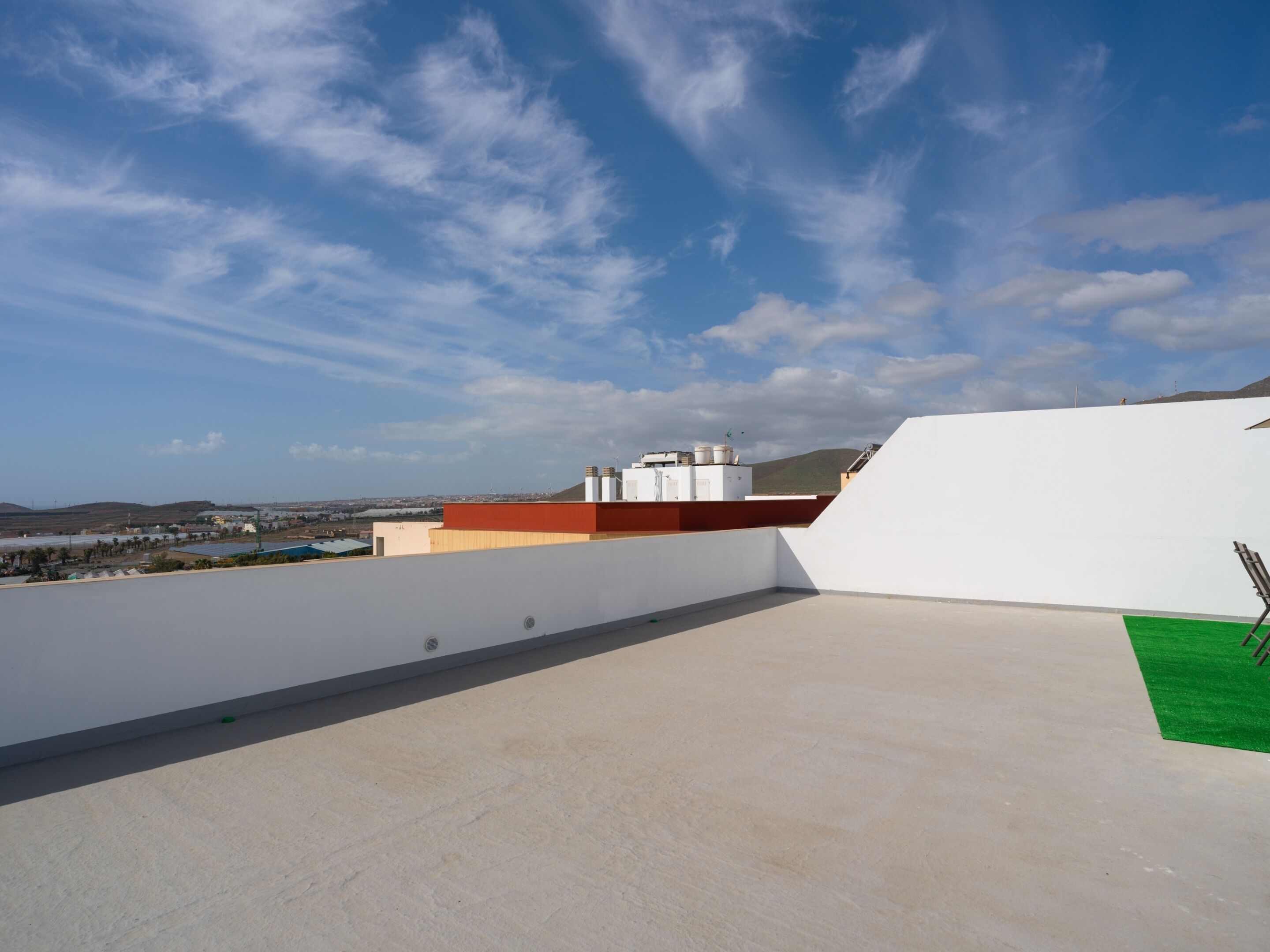 Eine Dachterrasse mit blauem Himmel, Blick auf entfernte Gebäude und einem Grünbereich.