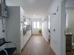 A modern kitchen with a refrigerator, oven, and microwave. There is a potted plant and a window with blinds.