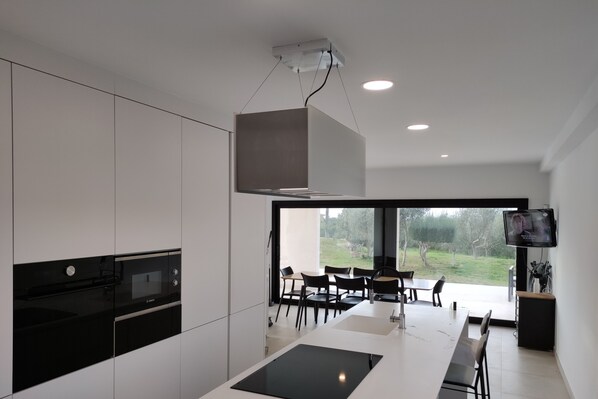 A modern kitchen with built-in appliances, a dining area with a large table and chairs, and a TV mounted on the wall. - Rural house with swimming pool, garden, barbecue, five minutes from the beach. (Muro)