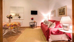 A living room with a dining table, a sofa, a TV, and a small table with a vase of flowers. - Lovely and cosy apartment nearby Navona Square (Roma)