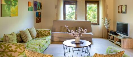 A living room with a green sofa set, a television, and artwork on the walls.