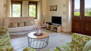 A living room with a sofa, a round coffee table with a vase of flowers, a flat-screen TV, and a wooden door with a view of the outdoors. - Villa Erontas Mini Pool and Heated Jacuzzi (Apokoronas)