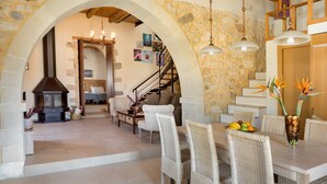 Amplia sala de estar con chimenea de piedra, una mesa de comedor con sillas de mimbre y una escalera que sube a un nivel superior.