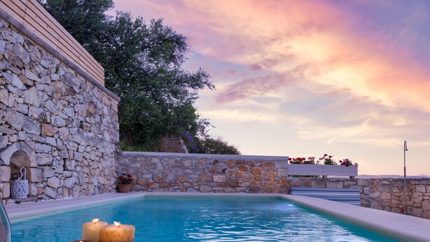 Una piscina de piedra con velas, rodeada de muros de piedra y una terraza de madera.