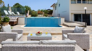 Un espace aménagé au bord de la piscine, avec des meubles en osier, une table sur laquelle sont disposés un panier de fruits et des boissons, et une piscine à l’eau d’un bleu limpide.