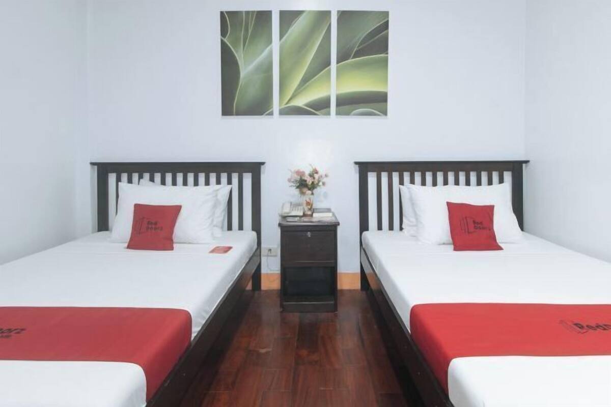 A hotel room with two single beds, a nightstand with a vase of flowers, and a wall-mounted artwork.