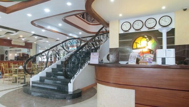 A hotel lobby with a curved staircase, a reception desk, and a clock display. - RedDoorz @ Nick Hotel Isabela (Alicia)