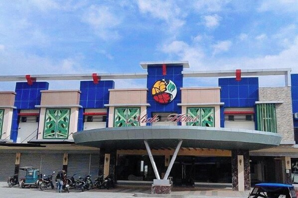 Un edificio con un logotipo distintivo, un acceso cubierto y un estacionamiento con vehículos.