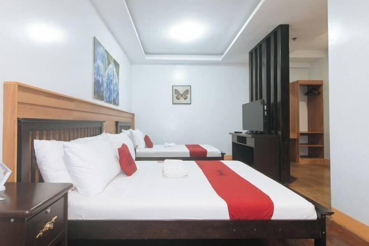 A hotel room with two beds, a desk, a wardrobe, and a television.