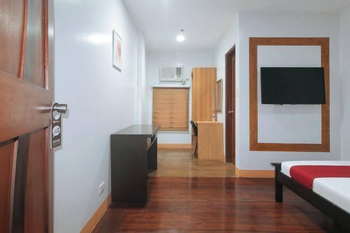A hotel room with a bed, a desk, a TV mounted on the wall, and a wooden wardrobe.