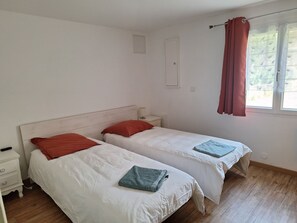 Una habitación con dos camas, una mesita de noche, una ventana con cortinas y una lámpara fijada a la pared.