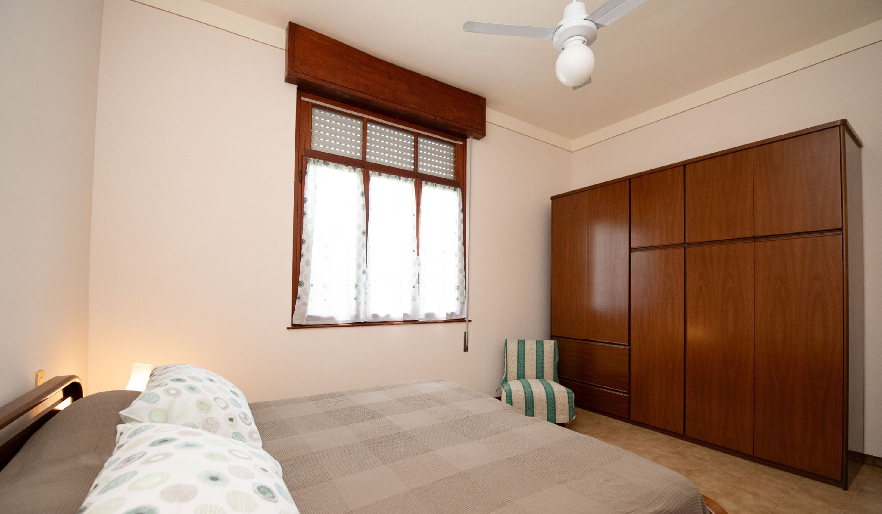 Un dormitorio con cama, armario, ventana con cortinas y ventilador de techo.