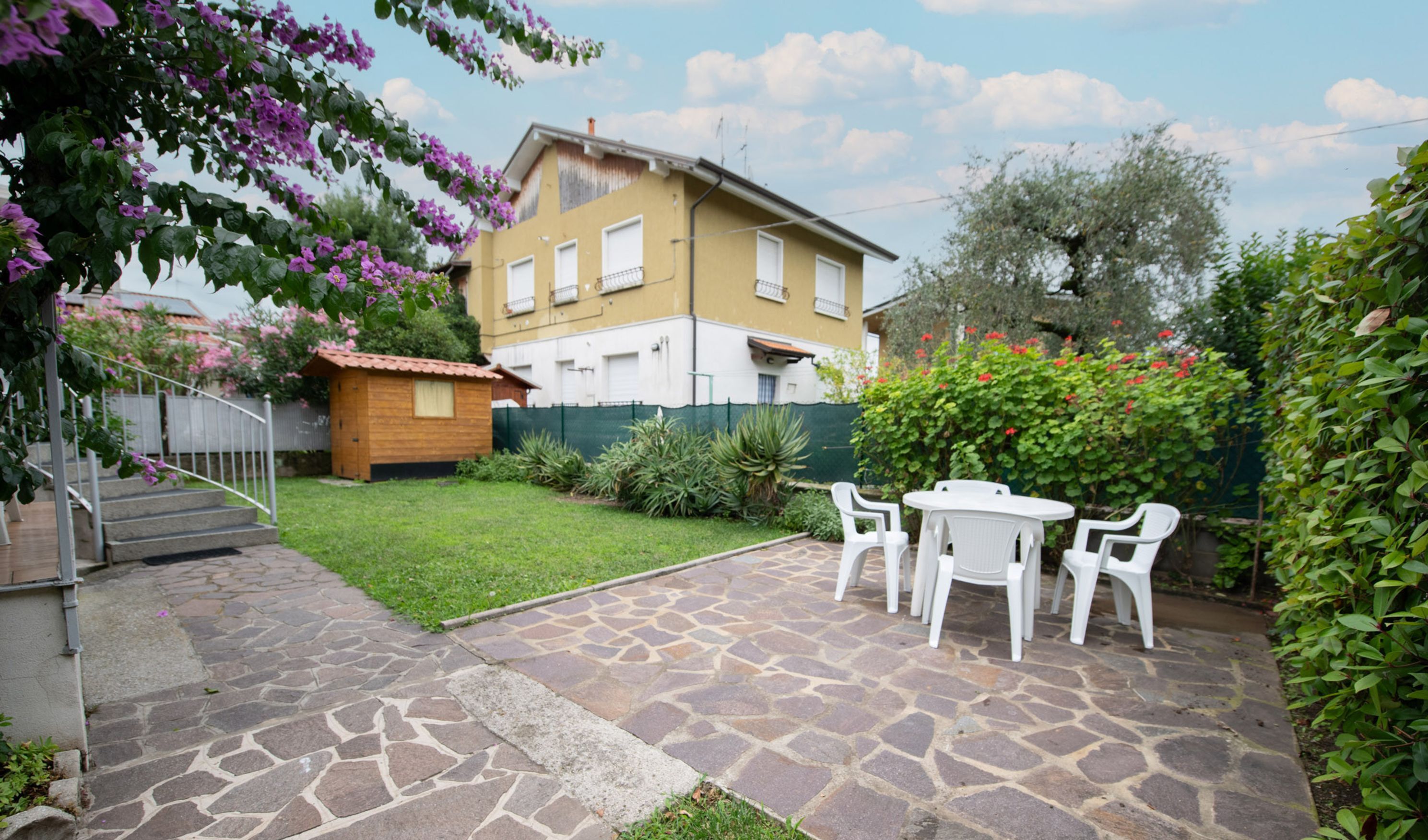 A courtyard with a stone patio, a small wooden shed, and a white table with chairs.