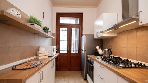 A modern kitchen with wooden cabinets, a stainless steel stove, and a built-in oven. There is a window with a wooden door and a plant on the shelf. - Villa Ada in Toscolano-maderno (Toscolano Maderno)