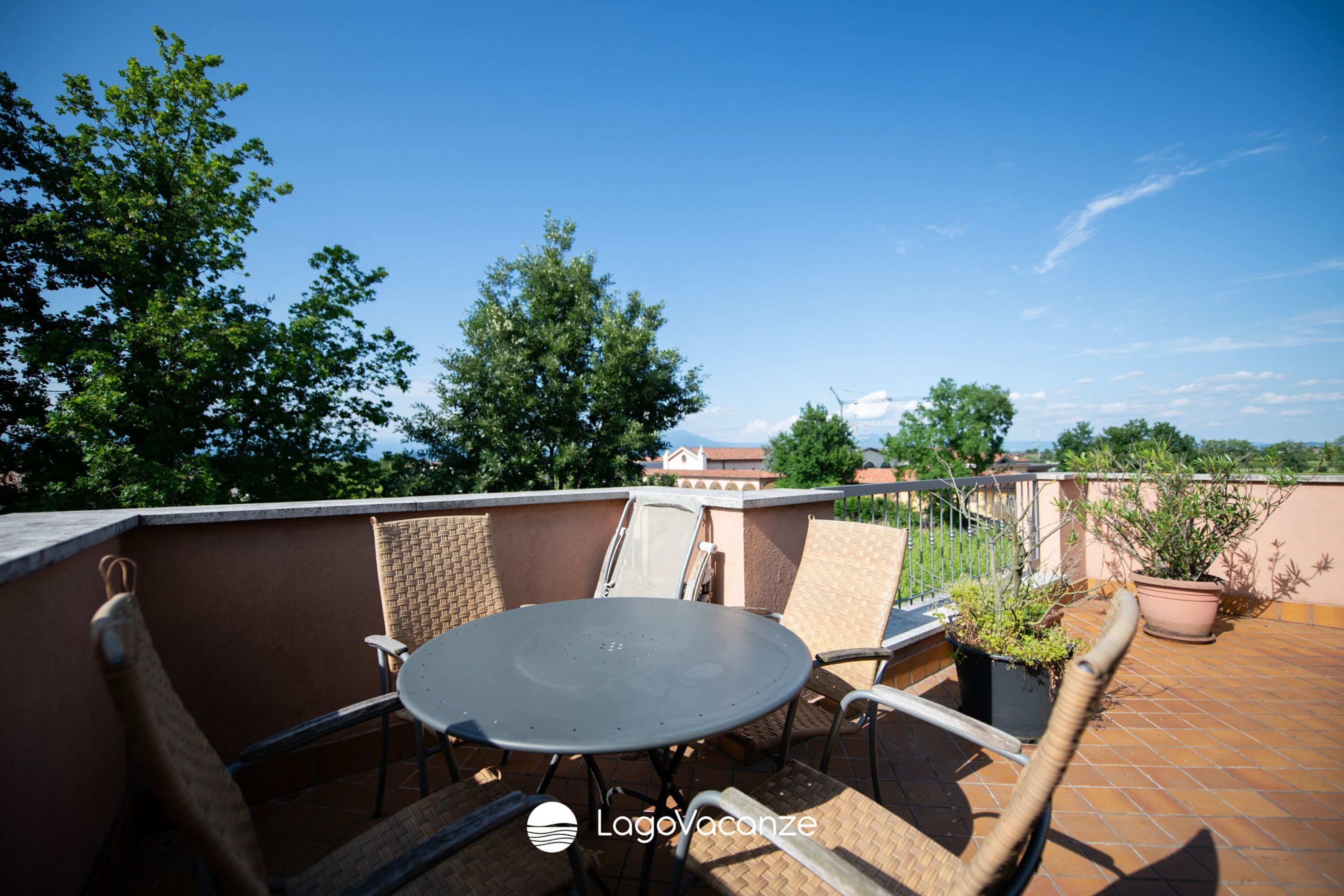 Una terraza en la azotea con una mesa redonda y sillas, plantas en macetas y vistas del paisaje urbano.