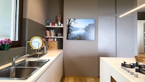 A modern kitchen with stainless steel sinks, a wooden floor, and a painting of a mountainous landscape. - Villa Anna Miralago in Puegnago sul Garda (Puegnago del Garda)
