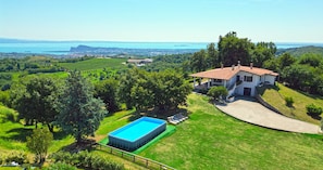 A house with a swimming pool surrounded by lush greenery and a view of a lake.