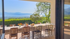 An outdoor dining area with a table set for two, overlooking a scenic landscape with mountains and a lake. - Villa Anna Miralago in Puegnago sul Garda (Puegnago del Garda)