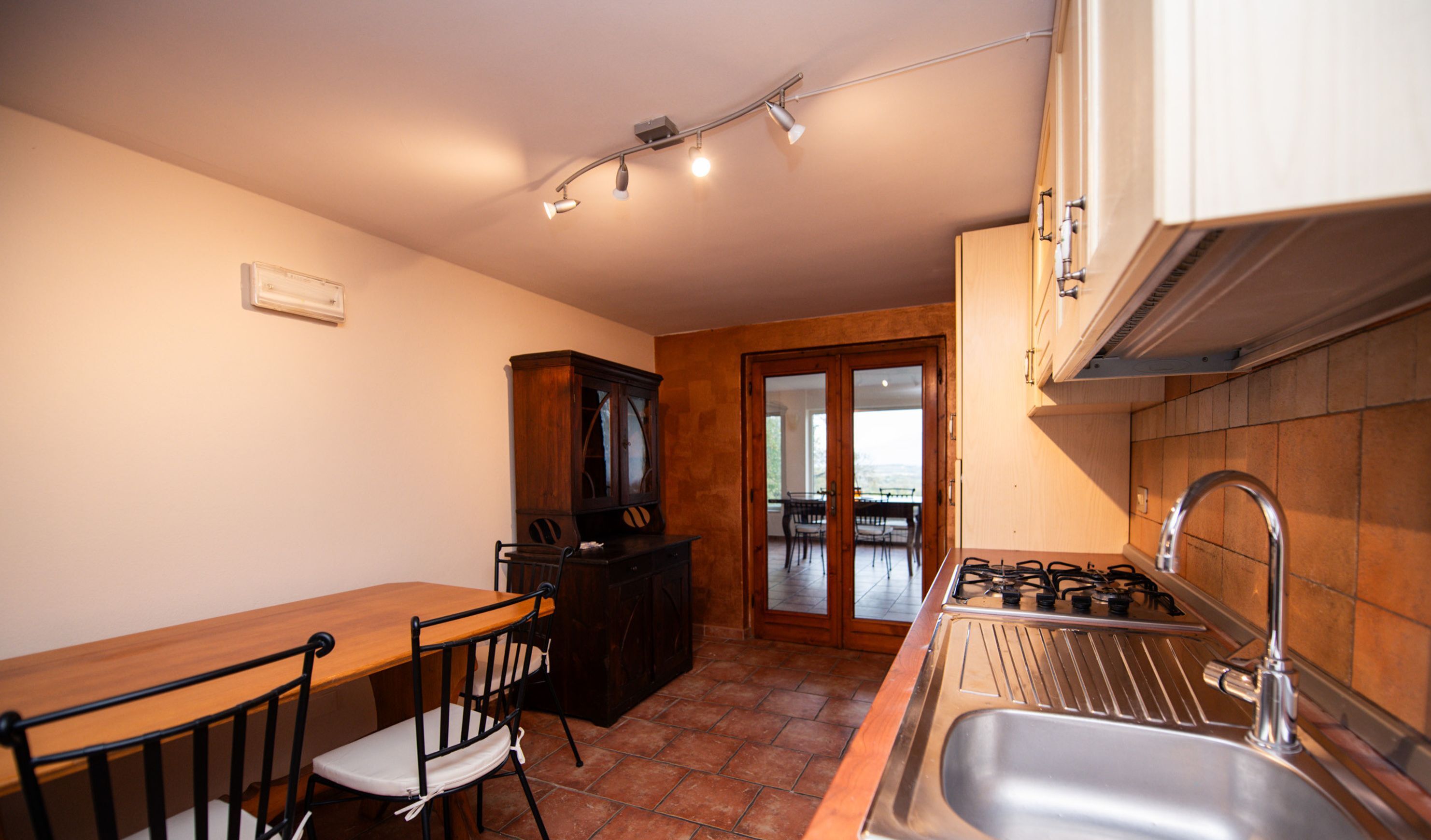 A compact kitchen with a dining table, chairs, a cabinet, and a sink.