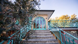 A staircase leading to a building with a turquoise arched entrance, a brick facade, and a green railing.
