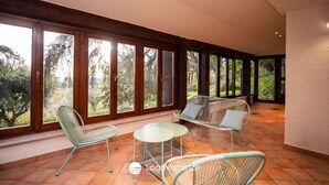 A spacious balcony with large windows, a seating area with chairs and a table, and a tiled floor.