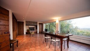 A dining area with a fireplace, a TV, and a large window overlooking a scenic view.