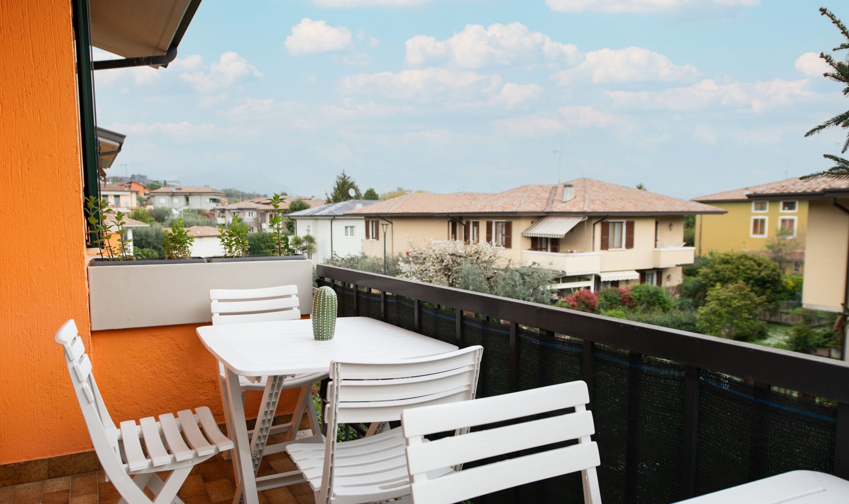 Un balcon avec une table et des chaises, un cactus et une vue sur les maisons voisines.