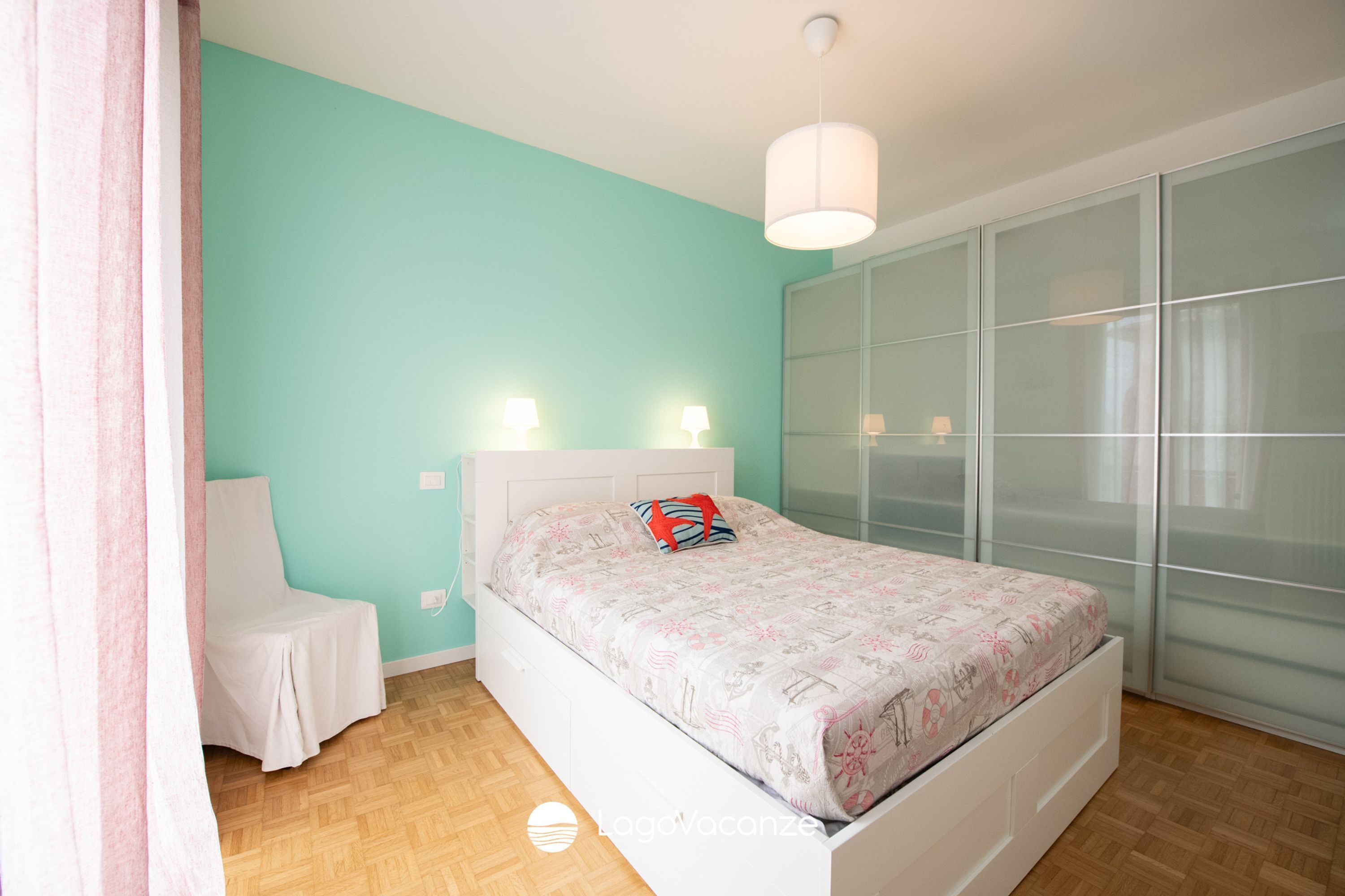 A bedroom with a bed, a chair, a wardrobe, and a hanging light fixture.