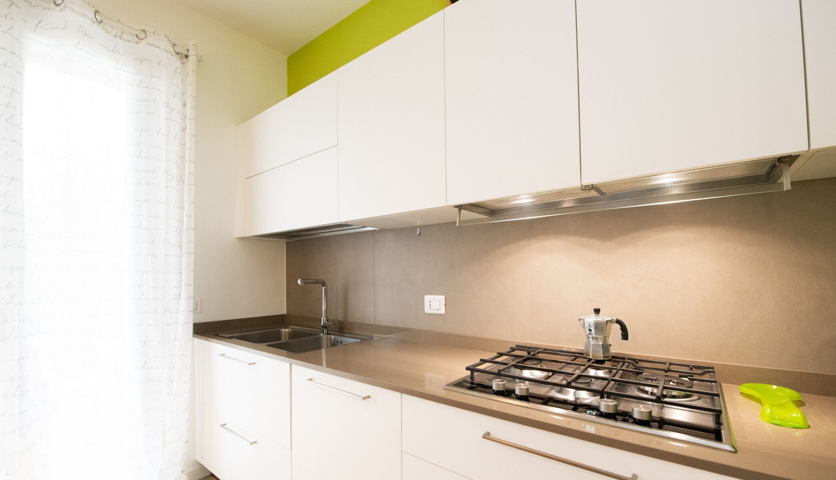 Une cuisine avec des armoires blanches, un évier en acier inoxydable et une cuisinière à gaz.
