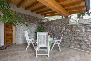 A covered patio area with stone walls and wooden beams, featuring a table and two white chairs. - Giardino dei Limoni in Toscolano-maderno (Toscolano Maderno)