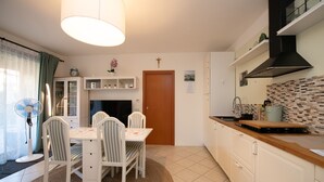 A modern kitchen with white cabinets, a wooden countertop, and a built-in stove. There is a dining area with a table and chairs, and a ceiling fan. - Villaggio Tavaredo - App 02 (Polpenazze del Garda)