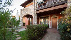 A stone building with a wooden balcony, a door, and a pathway leading to the entrance. - Villaggio Tavaredo - App 02 (Polpenazze del Garda)