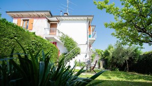 Una casa de dos pisos amb un balcó, una escala i un jardí.