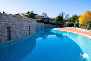 A swimming pool with stone walls and tiled flooring, surrounded by trees and buildings. - Borgo del Torchio - App H5 (Manerba del Garda)