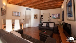 A living room with a wooden ceiling, a sofa, a TV, and a dining area with chairs and a table. - Borgo del Torchio - App H5 (Manerba del Garda)