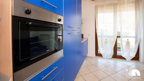 Eine Küche mit blauen Schränken, einem eingebauten Backofen und einem Fenster mit durchsichtigen Vorhängen.