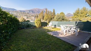 Eine Terrasse mit Gartenmöbeln, Blick auf eine Stadt und Berge, und ein grüner Zaun.