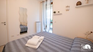 Ein Schlafzimmer mit Bett, Spiegel, einem Fenster mit Vorhängen, einem Regal mit Dekoration und einer Tür.