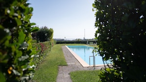 Una piscina con plataforma empedrada, rodeada de césped y setos cuidados.