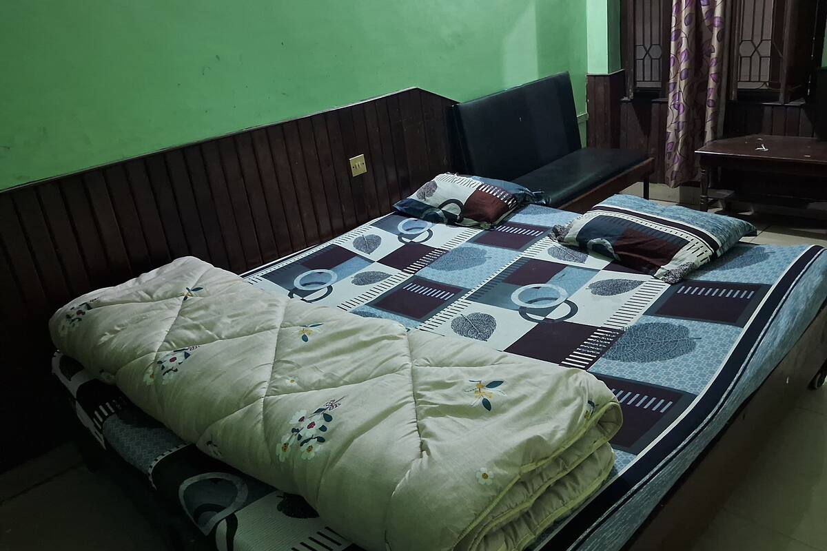A bed with a quilted cover and pillows, a wooden headboard, and a green wall.