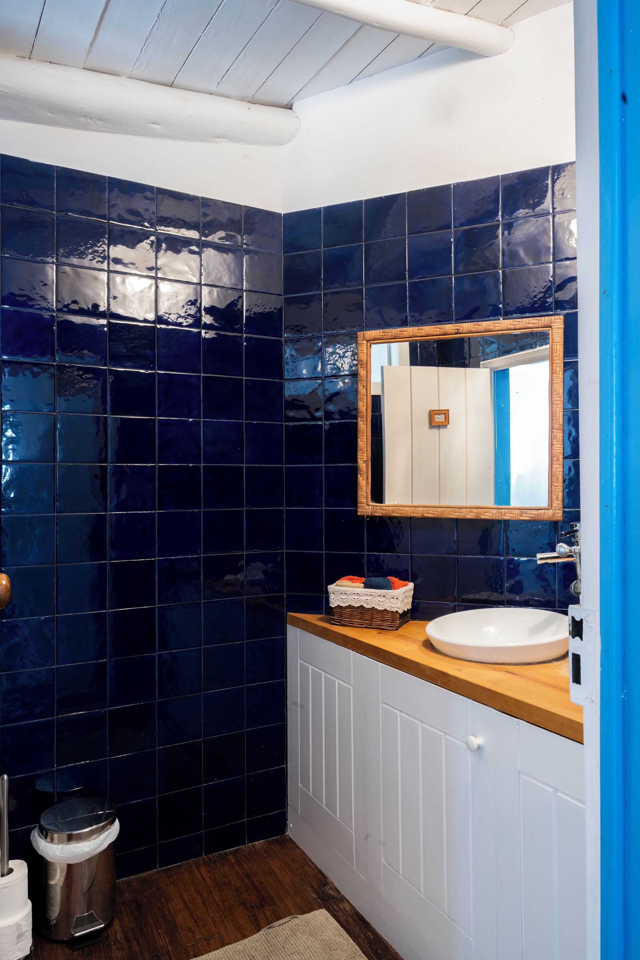 Een badkamer met donkerblauwe tegels, een houten aanrechtblad, een witte wastafel en een spiegel.