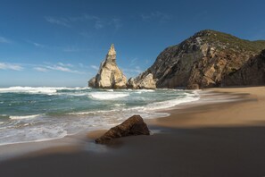 A beach with a large rock formation and a mountain in the background.