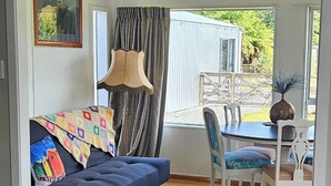 A cozy living room with a dark blue sofa, a dining table with chairs, and a view of a wooden deck and greenery outside. - Margs on The Corner
Home away from home
Nestled on the cycle trail (Kumara)
