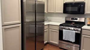 A kitchen with white cabinetry, a stainless steel refrigerator, a microwave, and a stove. - Spacious Waterfront Home for Groups (Stockton)